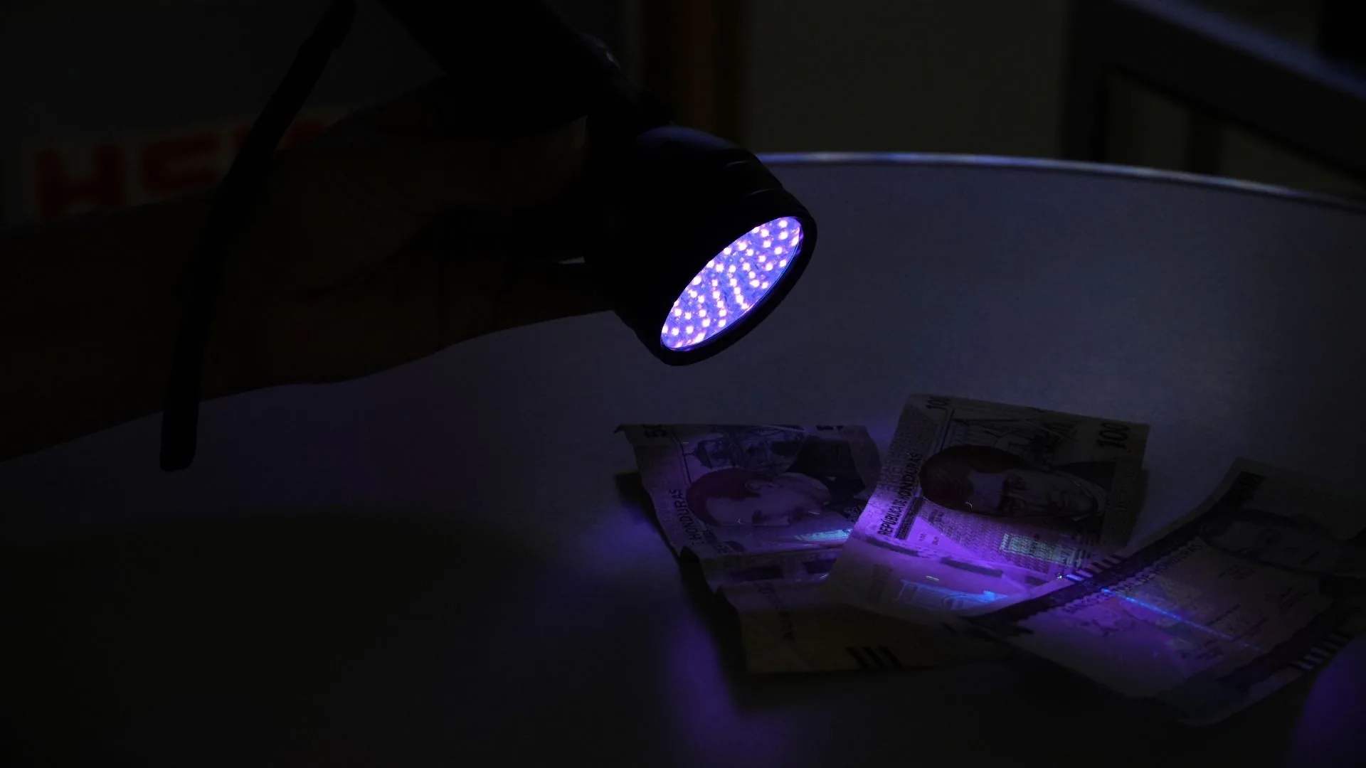Linterna UV para billetes encendida sobre varios billetes de lempira.
