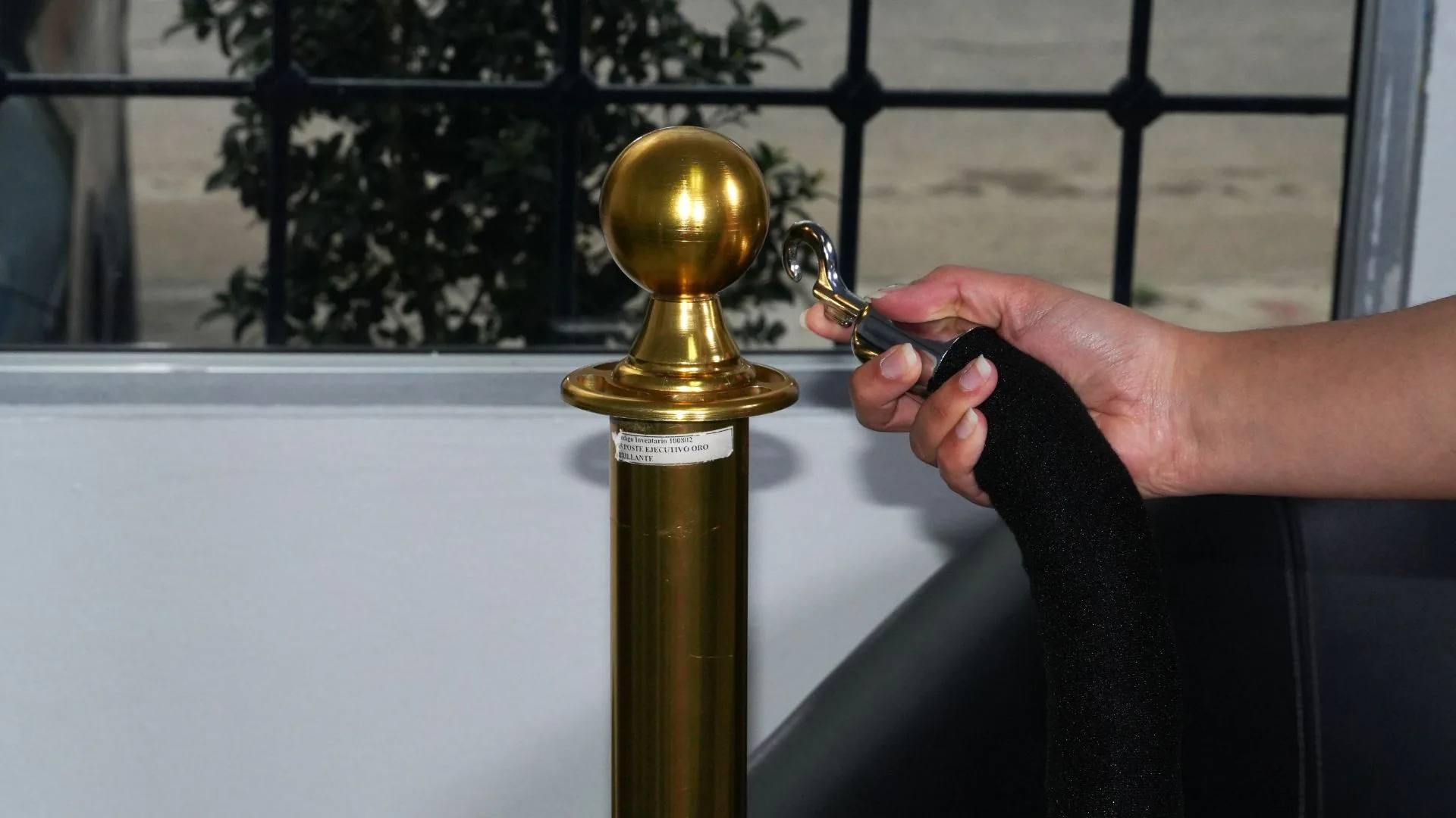 Gancho cromado del cordón de terciopelo junto al remate de un poste de fila ejecutivo dorado.