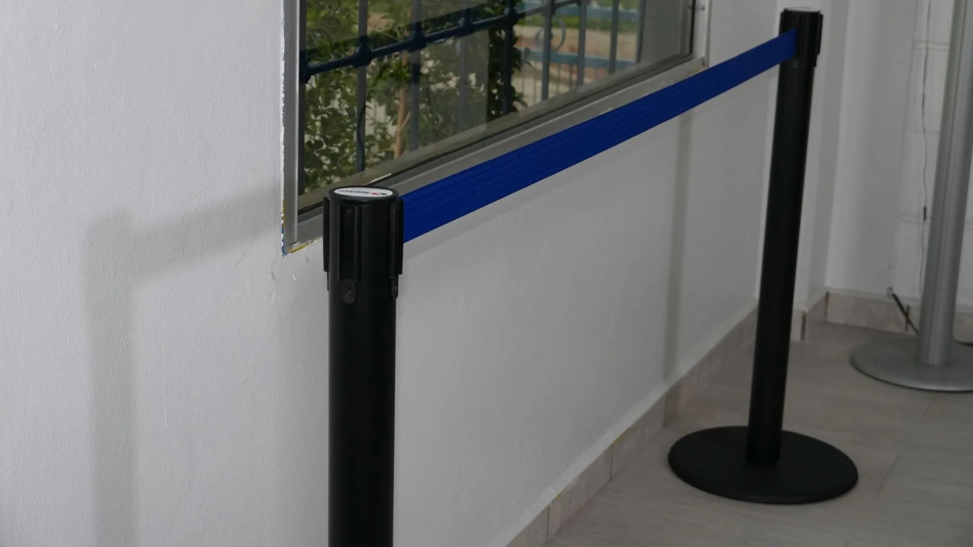 Dos postes de fila sencillos negros con la cinta azul extendida junto a una ventana.